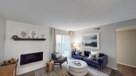 This single-floor residence offers a thoughtfully designed layout that balances comfort and functionality across its key living areas. The living room serves as the heart of the home, anchored by a striking white-painted brick fireplace with a dark wood mantle. Rich hardwood-style flooring, sliding glass doors, and vertical blinds fill the space with natural light and provide access to an outdoor balcony. The kitchen features white shaker-style cabinetry, a marble-look tile backsplash, stainless steel appliances including a full-size refrigerator, and a breakfast bar that connects seamlessly to the rest of the living area. Adjacent to the kitchen, the dining area accommodates a round table for four beneath a modern chandelier, with a sliding glass door that further extends the natural light throughout. Both bedrooms are finished with plush carpeting, neutral-toned walls, and generous windows dressed with curtain panels, creating restful and inviting retreats. The bathroom features wood-look tile flooring, gray vanity cabinetry with ample storage, a single basin sink, and a separate tub and shower area. Throughout the residence, textured ceilings and a cohesive neutral palette provide a clean, comfortable backdrop suited to a variety of lifestyles.