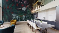 Located at 321 E Capital Street in Columbus, Ohio, this single-floor space makes an immediate impression through its bold and carefully curated design. The most striking feature is a dramatic, large-scale botanical mural that spans an entire wall, depicting an immersive nighttime nature scene complete with mushrooms, lush foliage, a butterfly, and vivid botanical details rendered in deep greens, purples, and reds. The mural serves as a commanding focal point that anchors the dining area.

The dining space centers around a substantial dark-topped table paired with cream upholstered chairs, accommodating a generous number of guests. Overhead, a gold-toned linear chandelier with candle-style lights adds warmth and a refined, contemporary elegance. Polished concrete flooring runs throughout, lending an industrial yet sophisticated character to the space.

Adjacent to the dining area, a modern kitchen features dark cabinetry, a matte black faucet, and integrated appliances including a stainless steel refrigerator. Clean white upper cabinetry and ample counter space complete the functional yet stylish layout. A mezzanine-level element is visible above, adding vertical dimension and architectural interest to the overall design. The space blends artistic expression with modern functionality in a cohesive, visually dynamic environment.
