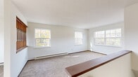 Located at 147 Chateau Hills in Parkersburg, West Virginia, this one-bedroom, one-bathroom residence offers a practical and well-organized single-floor layout. The living area is generously proportioned, featuring wall-to-wall carpeting, crisp white walls, and an abundance of natural light streaming through multiple large grid-pane windows that overlook the surrounding greenery. Baseboard heating units run along the exterior walls, ensuring year-round comfort. A classic wooden stair railing with turned spindles adds a traditional architectural detail to the space.

The kitchen is efficiently designed in an L-shaped configuration, showcasing rich dark wood cabinetry with ample upper and lower storage, light-toned countertops, a double-basin sink, a coil-top electric range, and tile flooring that contrasts neatly with the carpeted living areas.

The bedroom is a comfortable, carpeted retreat with clean white walls, warm wood-toned trim, and a large picture window that fills the room with natural light and outdoor views.

The full bathroom is well-appointed with a single vanity featuring wood cabinetry and a wide mirror, a full-size soaking tub and shower combination with chrome grab bars, and easy-to-maintain tile flooring. Overall, the space presents a clean, functional, and straightforward living environment.