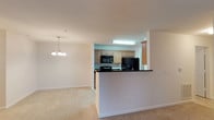 This renovated single-floor residence offers three bedrooms and two bathrooms across a thoughtfully designed layout. The open-concept living and dining area creates a welcoming atmosphere, anchored by plush carpeting underfoot and a decorative chandelier that adds a refined touch to the dining space. The kitchen is positioned at the heart of the home, featuring a convenient pass-through peninsula with dark countertops, light wood cabinetry, and black appliances including a refrigerator, microwave, and range. Overhead lighting in the kitchen ensures a bright, functional workspace. The half-wall peninsula creates a natural boundary between the kitchen and the living area while maintaining an open, connected feel throughout the shared spaces. The neutral color palette — from the soft beige carpeting to the clean white walls — provides a versatile backdrop that complements a variety of décor styles. The single-floor plan ensures easy accessibility and seamless flow between rooms. With its modern renovations and practical layout, this residence offers a comfortable and functional living environment suited for a range of lifestyles.