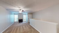 This renovated one-bedroom, one-bathroom unit in Ridgeland, Mississippi, offers a well-organized single-floor layout with a blend of updated finishes and practical design. The open living area is anchored by a wood-burning fireplace flanked by two windows, allowing natural light to fill the space. Plush carpeting covers the living and bedroom areas, while wood-look flooring runs through the kitchen, bathroom, and hallway, creating a clear visual distinction between zones. A ceiling fan with a light fixture is present in both the living area and bedroom, supporting air circulation throughout. A low half-wall with a white-painted rail divides the living space from the entry and dining transition area, adding subtle architectural definition. The kitchen features white shaker-style cabinetry, dark granite-look countertops, and a full suite of stainless steel appliances including a range, over-the-range microwave, dishwasher, and refrigerator. The bathroom includes a tub-shower combination with a curved curtain rod, wood-look flooring, and a vanity with dark countertops. The bedroom is a well-sized, carpeted room with a ceiling fan. A hallway connects the main living areas to the bedroom and bathroom, completing the efficient layout.