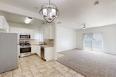 Located at 2825 S Lovers Ln in Visalia, California, this single-floor residence offers a clean, functional layout with a bright and neutral interior throughout. The kitchen is well-appointed with white cabinetry, tile backsplash, light tile flooring, and a full suite of stainless steel appliances including a gas range, over-the-range microwave, dishwasher, and refrigerator. A stylish orb-style chandelier illuminates the kitchen-dining area, which flows openly into the carpeted living room. The living room benefits from a ceiling fan and a sliding glass door that invites natural light and provides outdoor access. Multiple bedrooms are generously sized, each featuring plush carpet flooring, ceiling fans, and vertical-blind windows that allow for adjustable natural light. One bedroom includes a built-in closet and an additional door, likely leading to a private bath. The hallway connects the bedrooms through a central corridor equipped with a thermostat and overhead ventilation. Two bathrooms are present, each featuring tile flooring, white vanity cabinetry with marble-style countertops, a large mirror, and modern brushed nickel fixtures. An additional tiled room provides flexible utility space. The overall palette is crisp white with warm neutral tones, conveying a clean and move-in-ready atmosphere.