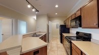 Located at 100 Estella Ct in Florence, Alabama, this single-story residence offers a well-organized layout with functional living spaces throughout. The kitchen is designed in a galley style, featuring warm wood cabinetry, light countertops, a double-basin sink, and black appliances including a refrigerator, range, and built-in microwave. Track lighting and recessed fixtures illuminate the space, which connects seamlessly to the open living and dining area. The living area is finished with rich hardwood-style flooring, crown molding, a pendant light fixture, and a ceiling fan, creating a comfortable and cohesive atmosphere. Multiple bedrooms carry the same hardwood-style flooring and are each equipped with ceiling fans and windows fitted with horizontal blinds that allow for natural light and outdoor views. The bathrooms are finished with tile flooring, wood vanity cabinetry, light countertops, large mirrors, and tub-shower combinations with brushed nickel fixtures. A dedicated laundry area includes wire shelving, a dryer vent connection, and an accessible electrical panel. Neutral wall tones throughout the home contribute to a clean, versatile aesthetic suitable for a variety of furnishing styles.
