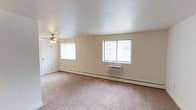 This single-floor residence offers a clean, functional layout designed for comfortable everyday living. The living area is generously sized, featuring soft wall-to-wall carpeting underfoot and multiple windows with vertical blinds that invite natural light throughout the day. A ceiling fan with integrated lighting keeps the space comfortable year-round, complemented by baseboard heating and a wall-mounted air conditioning unit for individual climate control.

The galley-style kitchen is a standout feature, lined on both sides with warm honey-toned wood cabinetry and granite-look countertops that provide ample storage and prep space. Black appliances, including a refrigerator, range, microwave, and dishwasher, offer a sleek contrast to the cabinetry, while durable tile flooring completes the practical design.

The bedrooms continue the carpeted aesthetic, each offering a calm, neutral palette with crisp white walls and clean white baseboards. Ceiling fans with light fixtures are present throughout, and windows with vertical blinds provide natural light and outdoor views. Individual wall-mounted climate control units ensure personalized comfort in each room. The overall ambiance of the space is bright, understated, and move-in ready, presenting a straightforward and livable environment.