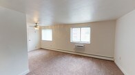 This single-floor residence offers a clean, functional layout designed for comfortable everyday living. The living area is generously sized, featuring soft wall-to-wall carpeting underfoot and multiple windows with vertical blinds that invite natural light throughout the day. A ceiling fan with integrated lighting keeps the space comfortable year-round, complemented by baseboard heating and a wall-mounted air conditioning unit for individual climate control.

The galley-style kitchen is a standout feature, lined on both sides with warm honey-toned wood cabinetry and granite-look countertops that provide ample storage and prep space. Black appliances, including a refrigerator, range, microwave, and dishwasher, offer a sleek contrast to the cabinetry, while durable tile flooring completes the practical design.

The bedrooms continue the carpeted aesthetic, each offering a calm, neutral palette with crisp white walls and clean white baseboards. Ceiling fans with light fixtures are present throughout, and windows with vertical blinds provide natural light and outdoor views. Individual wall-mounted climate control units ensure personalized comfort in each room. The overall ambiance of the space is bright, understated, and move-in ready, presenting a straightforward and livable environment.