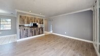 Located at 180 Royal Palm Dr in Kissimmee, Florida, this single-floor, 3-bedroom, 2-bathroom home offers a well-planned layout with a cohesive, neutral color palette throughout. The open-concept living, dining, and kitchen area forms the heart of the home, anchored by a striking peninsula with reclaimed wood-style paneling and bar seating. The living room features light wood-look tile flooring, a textured ceiling, crown molding, and a wall of mirrored panels flanking sliding glass doors that lead to a private balcony, filling the space with natural light and outdoor views. The galley-style kitchen is equipped with white cabinetry, marble-look countertops, black appliances, and tile flooring. The adjacent dining area includes a chandelier overhead. The three bedrooms feature wood-look tile flooring, textured ceilings, and ample natural light from windows with blinds. The primary bedroom is generously sized and includes dual closets for substantial storage. Additional closets throughout provide excellent organization. Both bathrooms are finished with white vanities, tile flooring, and clean, functional designs. A textured ceiling and crown molding details are consistent throughout, lending a cohesive, polished character to the entire home.