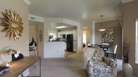 This single-story home showcases an open-concept floor plan that seamlessly integrates the living, dining, and kitchen areas into one cohesive space. The living room is carpeted and comfortably sized, featuring neutral-toned walls that create a warm, inviting atmosphere. A half-wall partition elegantly separates the living space from the kitchen without fully enclosing it, preserving the open feel throughout.

The kitchen is well-equipped with white cabinetry, black appliances including a full-size refrigerator, and a skylight overhead that draws in natural light, brightening the workspace. An arched passageway adds an architectural detail that contributes character and visual interest to the layout.

Adjacent to the kitchen, the dining area is defined by a stylish pendant light fixture and provides ample space for a full dining set. A window allows natural light to filter into this zone, enhancing the overall brightness of the shared space.

Throughout the home, the design balances practicality with aesthetic detail, featuring smooth ceilings with recessed vents, neutral finishes, and thoughtful transitions between areas that make the single-floor layout feel spacious and well-organized.