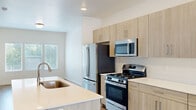 This thoughtfully designed three-story home offers 3 bedrooms, 3 bathrooms, and an attached garage across three well-proportioned floors. The ground level houses the garage, featuring a concrete floor, automatic opener, and direct interior access. The main living level is generously sized and centers around a contemporary kitchen outfitted with light wood cabinetry, white quartz countertops, stainless steel appliances including a gas range, over-the-range microwave, and a French door refrigerator. A peninsula with an integrated sink adds both workspace and casual dining potential. Light hardwood-style flooring flows throughout this level, complementing the bright, neutral palette. A pantry and living room complete this floor. The upper level hosts all three bedrooms, each filled with natural light from multiple windows offering views of surrounding greenery. The primary bedroom is a comfortable retreat with a walk-in closet featuring wrap-around hanging rails. The bathrooms are finished with tile flooring, wood-tone vanities, white quartz counters, and full tub-shower combinations. Each bedroom includes dedicated closet space. The home's clean, modern aesthetic is carried consistently throughout, creating a cohesive and livable environment.