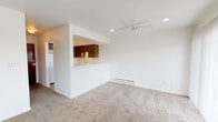 Located at 4500 Wilmington Pike in Kettering, Ohio, this single-floor residence offers a clean, functional layout designed for comfortable everyday living. The open living area is finished with plush wall-to-wall carpeting and features recessed lighting, a ceiling fan, and a baseboard heating unit. A half-wall pass-through seamlessly connects the living space to the kitchen, promoting an open and airy feel throughout. The kitchen is equipped with rich dark-wood cabinetry extending to the upper and lower levels, white countertops, a stainless steel sink, an under-cabinet range hood, and a dishwasher. Light-toned flooring in the kitchen provides a practical contrast to the carpeted living and sleeping areas. The bedroom is generously sized with carpeted flooring, a large window with blinds that allows natural light to fill the room, and a baseboard heating unit for year-round comfort. The bathroom area includes a wide vanity with a single sink, a large mirror, white cabinetry below, and an adjacent double-door closet finished in warm wood tones. The overall interior palette is crisp and neutral, with white walls throughout, creating a bright and welcoming atmosphere that provides a versatile canvas for personalization.