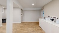 Located at 1000 N Donahue Dr in Auburn, Alabama, this shared laundry facility — known as the Club 34 Laundry Room — offers a clean, functional, and well-maintained space designed for convenience. The single-floor layout features warm-toned hardwood-style flooring throughout, complemented by neutral gray walls, white baseboards, and recessed lighting that creates a bright and welcoming atmosphere.

The room is equipped with a row of front-loading washing machines along one wall, each featuring digital control panels for ease of use. Stacked washer-dryer units are also available along an adjacent wall, maximizing the available footprint. A long, white folding table runs the length of one wall, providing ample surface area for sorting and folding laundry. A central support column anchors the space without disrupting the open flow.

Natural light enters through blinds-covered windows, adding to the well-lit environment created by the recessed ceiling fixtures. Posted signage outlines laundry room rules, ensuring a respectful shared experience. A trash receptacle is conveniently placed for users. The space is thoughtfully designed to serve a residential community efficiently, balancing practicality with a clean, modern aesthetic.