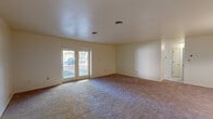 This single-story home in Chestertown, Maryland offers a well-organized layout with four bedrooms, two full bathrooms, and a dedicated laundry room. The living room is generously sized, featuring plush carpeting, neutral cream-toned walls, and a set of French doors that invite natural light and provide direct outdoor access. The carpet continues throughout the bedrooms, which are bright and spacious, with several rooms benefiting from large windows that frame views of the surrounding greenery. The primary bedroom offers a notably roomy footprint, providing ample space for furniture and personalization. The kitchen is designed in a U-shaped configuration with warm oak cabinetry, white countertops, a stainless steel sink, and a full suite of appliances including a dishwasher, range, and microwave. A window above the counter brings in natural light. Both bathrooms are finished with oak vanities, white countertops, tile flooring, and tub-shower combinations. A dedicated laundry room houses a full-size washer and dryer. Two closets and a hallway complete the floor plan. The home's consistent neutral palette and single-floor layout make it a practical and comfortable residence.