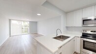 Located in North Miami Beach, this thoughtfully designed one-bedroom, one-bathroom residence offers a clean, contemporary aesthetic throughout. Light-toned luxury vinyl plank flooring flows seamlessly across the entire unit, complementing the soft gray-white walls and creating a bright, airy atmosphere.

The open-concept kitchen and living area serves as the heart of the home. The kitchen is outfitted with sleek, floor-to-ceiling white cabinetry, quartz countertops, a stainless steel undermount sink, and a full suite of stainless steel appliances including a refrigerator, range, and over-the-range microwave. A peninsula with additional counter space connects the kitchen to the living area, making it ideal for both cooking and entertaining. The living room opens directly to a private balcony through sliding glass doors, offering verdant outdoor views of palm-lined surroundings.

The spacious primary bedroom features soft neutral walls, generous natural light, and access to a dedicated closet with built-in shelving. The full bathroom is finished with a quartz-topped vanity, large wall mirror, and a tub-shower combination with clean white tile surround. Every detail of this residence reflects a modern, move-in-ready finish in a prime South Florida location.