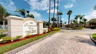 Treasure Cay Luxury Rental Apartments presents a polished first impression through its grand community entrance, marked by an elegant stone monument sign with gold lettering set against lush, manicured landscaping. The entry corridor is lined with towering palm trees that frame a decorative paver driveway, conveying a resort-inspired aesthetic consistent with Florida's upscale residential communities. The well-kept grounds feature vibrant red and green plantings alongside trimmed hedges, reinforcing the community's commitment to a refined outdoor environment. The single-story layout offers convenient, ground-level living. Unfortunately, the interior images provided are too underexposed to reveal specific details about the unit's rooms, finishes, or features. Based on what is visible, the community's exterior architecture reflects a Mediterranean-influenced design, with light-toned stucco buildings and tile roofing visible in the background. The overall ambiance of the community exterior is bright, open, and well-maintained, suggesting a carefully managed residential environment designed to offer comfort and a sense of exclusivity to its residents.