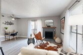 Located at 6585 McCallum Blvd in Dallas, TX, this well-appointed one-bedroom, one-bathroom unit offers a smartly designed single-floor layout that maximizes every square foot. The open-concept living, dining, and kitchen area forms the heart of the home, anchored by a striking gray brick fireplace with a warm wood mantel and sliding glass doors that open to a private balcony, flooding the space with natural light. Light-toned wood-style flooring runs throughout the main living area, complementing the neutral gray walls and textured ceilings. The kitchen features white cabinetry, stainless steel appliances, a gas range, and a peninsula breakfast bar with seating — ideal for casual dining. Floating shelves add a modern touch alongside the bar. A hallway leads to the bedroom, which is finished with plush carpet, a ceiling fan, and direct access to a dedicated walk-in closet. The full bathroom includes a tub-shower combination with white tile surround and a vanity with white cabinetry. In-unit laundry adds everyday convenience. The overall ambiance is clean, modern, and inviting — a practical yet stylish urban retreat in North Dallas.