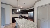 This single-floor residence offers a thoughtfully designed layout with modern finishes throughout. The kitchen serves as a central highlight, showcasing rich dark espresso cabinetry, granite countertops, a subway tile backsplash, and a full suite of stainless steel appliances including a side-by-side refrigerator, electric range, and built-in microwave. A large granite-topped kitchen island with an undermount sink provides additional prep space and casual dining potential, while pendant lighting overhead adds a polished touch. A dedicated wine rack built into the upper cabinetry adds a distinctive detail.

The open-concept living area transitions seamlessly from the kitchen, featuring wood-look hard flooring that gives way to plush carpeting in the main living space. Crown molding and gray accent baseboards provide clean architectural definition throughout.

The primary bedroom includes a ceiling fan, a double-door closet, and a window offering natural light. Its en-suite bathroom features granite countertops, a glass-enclosed shower, wood-look flooring, and access to a walk-in closet. A second bedroom, also carpeted with a ceiling fan and window, is served by a second full bathroom equipped with a soaking tub and shower combination. Additional storage closets are accessible near the kitchen area.