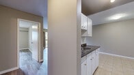 Located at 7155 Hall Rd in Surrey, BC, this single-floor, one-bedroom, one-bathroom residence offers a practical and comfortable layout. The open living room is a standout feature, showcasing light-toned laminate flooring, a classic white brick wood-burning fireplace, and a large sliding glass door that opens to a private balcony overlooking lush, mature greenery — flooding the space with natural light. A baseboard heating system runs along the perimeter of the living area. The galley-style kitchen is efficiently designed with white cabinetry accented by gold hardware, dark countertops, a white tile backsplash, tile flooring, and a full appliance package including a stove and refrigerator. Track lighting illuminates the workspace, and a dedicated pantry provides generous additional storage. The bedroom offers a comfortable footprint, continuing the laminate flooring and featuring a large sliding-door closet with built-in rod. The bathroom is finished with tile flooring, a marble-effect vanity countertop with under-sink storage, and a full tub-shower combination with tile surround. Throughout, neutral warm-grey tones and clean white trim give the space a cohesive, move-in-ready appearance.
