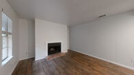 This efficient single-floor residence offers a thoughtfully arranged layout comprising a living room, kitchen, bedroom, bathroom, laundry area, and two closets. The living room makes an immediate impression with rich, dark wood-look flooring that extends throughout the main areas, crisp white walls, and a classic brick-hearth fireplace framed by a clean white surround — an inviting focal point for the space. Natural light filters in through double windows near the front entry, enhancing the bright, open feel of the room. The galley-style kitchen is outfitted with gray shaker cabinetry, white countertops, a stainless steel sink, and a white subway tile backsplash, offering ample storage and a clean, modern aesthetic. The primary bedroom is generously proportioned, featuring plush carpeting, a ceiling fan with lighting, and a sliding glass door that opens to a private balcony with outdoor views. The bedroom also benefits from a spacious walk-in closet with built-in shelving and hanging rods. The bathroom includes a full tub-shower combination with white tile surround and chrome fixtures. A dedicated laundry area and an additional closet round out the functional offerings of this well-designed home.