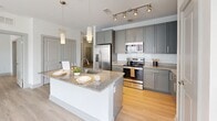 Located at 300 District Dr in Asheville, NC, this well-appointed 3-bedroom, 2-bathroom residence offers a thoughtfully designed single-floor layout. Light wood-style flooring flows seamlessly throughout, complementing the clean, neutral palette that defines the space.

The open-concept kitchen and living area serves as the heart of the home, featuring gray shaker cabinetry, granite countertops, a large central island with a built-in sink, stainless steel appliances, subway tile backsplash, and pendant lighting — all accented by track lighting overhead. A pantry provides additional storage convenience.

Each of the three bedrooms offers natural light through large windows with views of the surrounding neighborhood, and ceiling fans for year-round comfort. The generously sized primary bedroom includes a walk-in closet outfitted with wire shelving systems. Additional closets are plentiful throughout the unit, totaling five in all.

The two bathrooms mirror the kitchen's refined aesthetic, featuring gray shaker vanities, granite countertops, large framed mirrors, and dark tile-surround tub/shower combinations. A sliding glass door in one area of the residence provides outdoor access, adding to the bright, airy feel of this well-organized and modern home.
