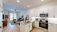 Located at 15621 Bovis Way in Fort Worth, TX, this one-bedroom, one-bathroom residence offers a thoughtfully designed open-concept layout that maximizes every square foot. The kitchen is a standout feature, showcasing crisp white shaker cabinetry, granite countertops, a center island with an undermount sink, and a full suite of stainless steel appliances including a refrigerator, electric range, microwave, and dishwasher. Light wood-style flooring flows seamlessly from the kitchen into the living room, which is bathed in natural light from large French doors that open to views of the exterior courtyard. A ceiling fan adds comfort to the living area. The bedroom offers a serene retreat with plush carpeting, a ceiling fan, natural light from a window, and a bold accent wall. It connects directly to the full bathroom, which features granite countertops, an undermount sink, a tub-shower combination, and direct access to a walk-in closet with built-in shelving. The exterior of the community presents an attractive blend of stone and board-and-batten siding, reflecting a modern farmhouse aesthetic. Clean, neutral tones and recessed lighting throughout the residence contribute to a bright, contemporary ambiance.
