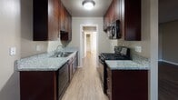 This single-floor unit offers a thoughtfully designed layout with a blend of practical features and modern finishes throughout. The open living and dining area is anchored by rich wood-look flooring that extends through the main spaces, complemented by neutral-toned walls and a textured ceiling with a ceiling fan overhead. Natural light filters in through a sliding glass door, while a wall-mounted A/C unit adds functional convenience near the entryway.

The galley-style kitchen is efficiently designed with rich, dark wood cabinetry lining both sides, granite countertops, a stainless steel sink, and black stainless appliances including a gas range and built-in microwave. The kitchen opens toward the living area, creating a connected flow.

The bedrooms are carpeted for comfort, with one featuring a sliding glass door that invites natural light and a mirrored closet. Another bedroom includes a walk-in closet and direct access to a well-appointed bathroom showcasing a dual-sink vanity with granite countertops, rich wood cabinetry, and a large framed mirror. A full bathroom with a combination tub and shower, wood-look flooring, and matching finishes completes the space. The overall ambiance is clean, neutral, and move-in ready.