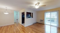 This single-floor residence at Queens Gate, 111 Espresso, is designed with a practical and cohesive layout that emphasizes comfort and functionality. Warm-toned hardwood floors extend throughout the main living areas, lending a consistent and polished aesthetic across each room.

The spacious living area serves as the heart of the unit, featuring a ceiling fan with light fixture, a wall-mounted air conditioning unit, and a sliding glass door that opens to a private balcony with outdoor views. A pass-through window connects the living space to the kitchen, maintaining an open feel while clearly defining each area.

The kitchen is outfitted with dark espresso cabinetry, granite-style countertops, a decorative tile backsplash with mosaic accent strips, and black appliances including a gas range, dishwasher, and refrigerator, complemented by a stainless steel microwave. Natural light enters through a window above the cooking area.

The bedrooms continue the hardwood flooring and are well-lit by windows, with ceiling fans and baseboard heating providing year-round comfort. Additional rooms offer flexible use and maintain the same clean, neutral palette.

The bathroom features floor-to-ceiling beige tile, a glass-enclosed tub and shower combination, a vanity with framed mirror, and a natural light source via a windowed wall. Overall, the unit presents a clean, move-in-ready environment.