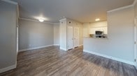 This single-floor residence offers a thoughtfully designed layout that balances comfort and functionality. The open living area is anchored by durable wood-look flooring, neutral gray walls, and crown molding, creating a clean and modern aesthetic. Multiple windows with horizontal blinds allow natural light to flow freely throughout, offering views of the surrounding greenery.

The kitchen is a standout feature, equipped with white shaker-style cabinetry, granite countertops, a mosaic tile backsplash, and a full suite of stainless steel appliances including a range, over-the-range microwave, refrigerator, and dishwasher. A breakfast bar provides additional counter space and serves as a natural transition between the kitchen and the main living area. A louvered closet door nearby offers convenient pantry or utility storage.

The bedrooms are comfortably sized, each featuring plush carpet flooring, ceiling fans with light fixtures, and windows that bring in natural light. At least one bedroom includes a walk-in closet with built-in hanging rods. The bathroom is finished with a full-size tub and shower combination set against clean white tile surround with chrome fixtures, providing a bright and functional space.