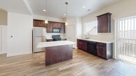 This two-story home in Lehi, Utah offers a thoughtfully designed layout spread across two floors. The main level welcomes you with a bright, open living room featuring light hardwood-style flooring, elegant wainscoting, vertical blinds allowing ample natural light, and a ceiling fan for year-round comfort. The kitchen is a standout, outfitted with rich dark wood cabinetry, white countertops, a central island, gas range, stainless steel refrigerator, and a double sink beneath a window — all tied together with coordinating hardwood-style flooring. A convenient half bathroom is also located on the main floor. Upstairs, two carpeted bedrooms offer comfortable retreats, each with access to closet space. The spacious primary bedroom features a walk-in closet with built-in shelving and hanging rods, providing generous storage. The bathrooms are finished with wood-toned cabinetry, light countertops, and clean white fixtures, including a tub-shower combo. Neutral tones, white trim, and wainscoting details carry throughout, creating a cohesive and inviting aesthetic. The home's clean design and practical layout make it a well-rounded living space in the Traverse Towns community.