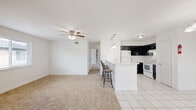 This thoughtfully designed 2-bedroom, 2-bathroom single-floor residence offers a functional and comfortable layout throughout. The open-concept living and kitchen area serves as the heart of the home, where light-toned carpet flows seamlessly into tile flooring at the kitchen's edge. The kitchen is equipped with dark cabinetry contrasted against white appliances and a granite-topped peninsula breakfast bar with seating for three, illuminated by a trio of pendant lights — ideal for casual dining or entertaining. A separate living area features plush carpeting, a ceiling fan with light fixture, and a corner fireplace framed in neutral stone tile, creating a warm and inviting atmosphere. Natural light filters in through multiple windows fitted with blinds. The primary bedroom offers a generous footprint with bright white walls and soft carpet, while the second bedroom provides double bi-fold closet storage and convenient proximity to in-unit washer and dryer connections. Both bathrooms are finished with classic white tile flooring and tub-shower combinations. Throughout the residence, a clean, neutral palette and consistent finishes create a cohesive and move-in ready environment.