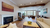 Located at Berkley Manor in Cranberry Township, PA, this well-appointed single-floor community clubhouse offers a generous and versatile layout designed to serve residents across a range of needs. The welcoming living room features light hardwood flooring, recessed lighting, a classic fireplace with a white mantel, crown molding, and large French doors that invite abundant natural light. An expansive open area flows seamlessly into a modern kitchen outfitted with rich wood cabinetry, granite countertops, a tile backsplash, stainless steel appliances, and a large island with bar seating for multiple guests. A second, more casual lounge area continues the hardwood flooring and open feel, with oversized windows offering views of the surrounding greenery. The dedicated fitness center is thoroughly equipped with treadmills, stationary bikes, ellipticals, a full dumbbell rack, benches, and floor-to-ceiling mirrors paired with mounted flat-screen TVs. Two private office spaces provide quiet workstations with L-shaped desks and patterned carpet, while a smaller conference-style room with a round table and natural window light offers an ideal setting for small meetings. Multiple hallways connect each area efficiently throughout the space.
