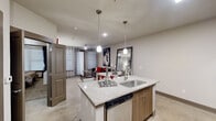This two-bedroom, two-bathroom unit at 14805 Grisby Road in Houston's Energy Corridor district is thoughtfully designed to maximize its compact single-floor layout. The open-concept kitchen serves as a central hub, featuring a granite-topped island with an undermount sink, pendant lighting, and bar seating. Walnut-toned cabinetry lines the walls alongside a full suite of stainless steel appliances, including a refrigerator, range, and microwave. Concrete-style flooring extends throughout the main living areas, lending a clean, contemporary feel.

A hallway connects the two bedrooms and bathrooms, maintaining a clear sense of organization within the floor plan. The primary bedroom accommodates a queen or full-sized bed and includes a ceiling fan, carpeted flooring, and a window with blinds and draping that allows for natural light control. The second bedroom follows a similar layout and feel.

Both bathrooms are well-appointed; one features a deep soaker tub surrounded by large-format tile, while the other includes a granite-topped vanity with wood-grain cabinetry. A dedicated closet provides additional storage. Neutral warm-gray tones used throughout the unit create a cohesive, modern aesthetic.