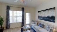 This well-designed 2-bedroom, 2-bathroom residence offers comfortable single-floor living across a generously sized floor plan. The living area serves as the heart of the home, featuring plush carpeting, a ceiling fan, and large windows that flood the space with natural light. A glass-paneled door provides access to the outdoors, enhancing the bright and airy atmosphere. Neutral wall tones create a versatile backdrop, complemented by tasteful décor including bold blue accent pieces and contemporary wall art. The layout is thoughtfully arranged to maximize functionality and flow between living spaces. The two bedrooms offer private retreats, each supported by a dedicated full bathroom, making this layout ideal for roommates, guests, or a home office setup. The overall ambiance is warm and inviting, with an emphasis on natural light and open, comfortable living. This residence combines practical design with welcoming interiors, delivering a balanced living experience suited to a variety of lifestyles.