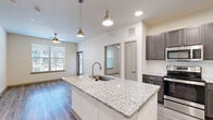 This 2-bedroom, 2-bathroom residence offers a thoughtfully designed single-level layout that makes efficient use of its space. The open-concept living and kitchen area serves as the heart of the home, featuring light wood-style flooring, recessed lighting, and a ceiling fan. The kitchen is highlighted by a central island with a granite countertop and undermount sink, complemented by rich dark cabinetry, stainless steel appliances including a refrigerator, range, and built-in microwave, and stylish pendant lighting overhead. Natural light flows in through windows fitted with blinds, creating a bright and welcoming atmosphere.

Both bedrooms are carpeted and offer a quiet, comfortable retreat, with the second bedroom featuring dual windows that invite additional natural light. Each room includes access to a dedicated closet for ample storage. The two bathrooms are finished with granite-topped dark vanities, undermount sinks, brushed nickel fixtures, and large mirrors. The primary bathroom includes a glass-enclosed walk-in shower with tile surround, while the second bathroom offers similar upscale finishes. A connecting hallway ties the layout together, providing smooth circulation throughout the residence.