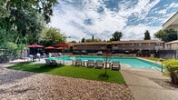 Located at 929 Nord Avenue in Chico, California, this outdoor community pool area offers a well-appointed recreational retreat designed for relaxation and leisure. The centerpiece of the space is a generously sized swimming pool with clear turquoise water, framed by a clean concrete pool deck that provides ample room for lounging and socializing.

Surrounding the pool, multiple lounge chairs and seating areas are arranged for comfort, shaded by a series of distinctive red patio umbrellas that add a vibrant pop of color to the setting. The pool area is further enhanced by the presence of mature, towering trees that line the perimeter, offering natural shade and a sense of seclusion while contributing to the lush, park-like ambiance of the space.

A dedicated outdoor entertaining area is also visible, complete with seating, tables, and what appears to be a barbecue station, making it well-suited for gatherings. The pool area is enclosed by a secure fence, ensuring privacy and safety for residents. The multi-unit residential buildings nearby feature a traditional stucco and earth-tone exterior, complementing the outdoor environment. The overall setting reflects a community-oriented design that balances functionality with a relaxed, California outdoor lifestyle.