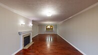 This single-floor space is characterized by rich, deep-toned hardwood flooring that flows consistently through the main living areas, bedrooms, and connecting hallways, lending warmth and visual continuity throughout. The spacious living room is a standout, anchored by a stone-surround fireplace with a classic white mantle and decorative tile hearth. Crown molding and a textured ceiling add architectural detail, while wall sconces and a central ceiling fixture provide ambient lighting. An arched pass-through opening connects the living area to the adjacent dining space, which features a pendant chandelier and views into the kitchen.

The kitchen is well-equipped, showcasing raised-panel wood cabinetry extending to the ceiling, granite countertops, a mosaic tile backsplash, recessed lighting, and stainless steel appliances including a gas range, built-in microwave, and dishwasher. Tile flooring grounds the space practically.

A bright secondary room offers multiple windows with views of the surrounding neighborhood and access to a door, allowing natural light to fill the area. Bedrooms are connected by hardwood hallways and supported by two bathrooms. One bathroom features a corner soaking tub, single vanity with wood cabinetry, and a separate shower. The second bathroom offers a full tub-shower combination and a matching wood vanity with ample storage.