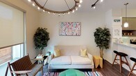 This single-floor residence offers a thoughtfully designed layout that balances contemporary finishes with an eclectic, colorful aesthetic. The entry introduces large sliding glass doors that open to a private balcony, allowing natural light to flow into the interior.

The living area serves as a central gathering space, anchored by a striking circular chandelier with exposed Edison bulbs. Warm hardwood-style flooring runs throughout, complemented by vibrant artwork and lush indoor plants that enliven the atmosphere.

The kitchen is outfitted with stainless steel appliances, including a gas range, built-in microwave, and French door refrigerator. Taupe cabinetry pairs with granite countertops extending along a breakfast bar illuminated by pendant lighting, creating an open, functional workspace.

A dedicated hallway connects to a stacked washer and dryer unit for in-unit laundry convenience. The primary bedroom features plush carpeting, a walk-in closet with built-in shelving, and an elegant chandelier. A secondary bedroom includes its own statement chandelier, roller shade window treatments, and a colorful chevron-patterned dresser. The bathroom is finished with large-format neutral tile surrounding a soaking tub and rain showerhead.