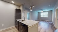 This well-appointed single-floor residence offers a cohesive modern aesthetic defined by neutral gray tones, hardwood-style flooring, and consistent granite countertop finishes throughout. The open-concept kitchen serves as a central hub, featuring a large island with a granite surface and undermount sink, dark espresso cabinetry, pendant and track lighting overhead, and black appliances including a refrigerator, range, and dishwasher. The kitchen flows seamlessly into the living area, which benefits from a ceiling fan and natural light filtering through blinds, creating a bright and airy atmosphere. The bedrooms are generously sized, each equipped with ceiling fans and large windows fitted with blinds that allow for ample natural light and outdoor views. The primary bathroom is finished with a granite-topped dark vanity, dual medicine cabinet mirrors, and direct access to a walk-in closet complete with wire shelving. A second full bathroom mirrors the same design language, featuring a granite vanity, dark cabinetry with overhead storage, and a tub-shower combination. Consistent flooring, clean white trim, and thoughtful lighting tie every room together into a cohesive, move-in-ready living space.