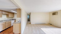 Located at 4453 Chestnut Ridge Rd in Amherst, NY, this single-floor, two-bedroom unit offers a practical and comfortable layout across a well-utilized floor plan. The living room is a bright, open space featuring wall-to-wall carpeting, a baseboard heating unit, a wall-mounted air conditioner, and a large sliding glass door framed by vertical blinds that floods the room with natural light and provides access to an outdoor patio area with green views. The galley-style kitchen is efficiently designed with warm, light wood cabinetry lining both sides, granite-look countertops, a stainless steel sink, hardwood-style flooring, and white appliances including a range and refrigerator, all illuminated by a ceiling skylight panel. The spacious primary bedroom features neutral carpet, warm beige walls, a baseboard heater, a window with blinds for natural light, and a closet with bifold doors. The second bedroom is similarly appointed with soft carpet, a baseboard heater, and a large double window that brings in generous daylight. Both bedrooms include panel doors and clean white trim throughout. The overall palette of warm beige tones and neutral finishes creates a calm, cohesive ambiance throughout the unit.