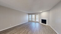 This two-story, two-bedroom, three-bathroom home offers a thoughtfully organized layout split evenly across two floors. The main level features an open living room with wood-look plank flooring, a classic white-mantled fireplace, and a glazed door with flanking windows that invite natural light and outdoor access. Adjacent to the living area is a galley-style kitchen outfitted with white cabinetry, white countertops, stainless steel appliances including a refrigerator, range, and built-in microwave, and light hardwood-style flooring. A hallway connects the main living spaces and includes convenient closet storage. The bathrooms are finished with white vanities, chrome hardware, and wood-look tile flooring; at least one features a full tub-shower combination. Upstairs, the two bedrooms are carpeted in neutral tones, providing a comfortable retreat. The generously sized primary bedroom features dual mirrored sliding closet doors offering ample storage. The second bedroom is bright and versatile. Neutral gray walls, white trim, and consistent flooring choices throughout create a clean, cohesive aesthetic that is both practical and inviting.