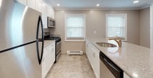 This single-floor residence offers a thoughtfully designed layout that blends comfort and functionality throughout. The spacious living area greets you with rich hardwood flooring, recessed lighting, and crown molding, creating a warm and polished atmosphere. A sliding glass door floods the space with natural light and provides easy outdoor access. The open-concept design flows seamlessly into the kitchen, where white shaker-style cabinetry, granite countertops, and a suite of stainless steel appliances — including a gas range, microwave, refrigerator, and dishwasher — make for an efficient and attractive cooking space. A peninsula with an undermount sink adds additional prep and seating space. Travertine tile flooring and dual windows with blinds complete the kitchen's bright, clean aesthetic. The bedroom features hardwood floors, crown molding, a ceiling fan, and a window overlooking the exterior, along with a wall-mounted HVAC unit for individualized climate control. The full bathroom is finished with travertine tile flooring, a tub-shower combination with tiled surround, and a dark-toned vanity with a white countertop. A second bathroom, accessed from the hallway, mirrors the same quality finishes with matching tile flooring, a dark vanity, and a window for natural ventilation. Baseboard heating is present throughout the unit.