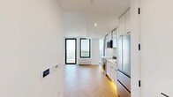 Located at 104 Fleet Pl in the heart of Downtown Brooklyn, this thoughtfully designed two-bedroom, one-bathroom residence offers a refined modern aesthetic throughout. Warm herringbone-patterned hardwood flooring flows seamlessly across the entire unit, lending a sophisticated character to every room.

The open kitchen is outfitted with sleek white cabinetry — including glass-front upper cabinets — stainless steel appliances, a built-in microwave, and clean white countertops accented by matte black hardware, all illuminated by recessed lighting above.

Both bedrooms are bright and airy, benefiting from large, black-framed floor-to-ceiling windows that frame expansive views of the Brooklyn skyline and surrounding cityscape. The primary bedroom features generous closet space with dual built-in closets, while the second bedroom offers the same elegant flooring and clean white walls.

The bathroom is finished with a spa-inspired design, showcasing vertically stacked mosaic tile surrounds, a deep soaking tub with overhead shower, a wall-mounted wood-toned vanity with an integrated sink, and terrazzo-style flooring that ties the refined aesthetic together.

The living and entry areas are open and versatile, completed with the same herringbone floors and recessed lighting for a cohesive, contemporary feel throughout.