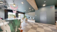 Located in Nashville's vibrant Wedgewood-Houston neighborhood, this thoughtfully designed amenity space serves as a dynamic community hub. The interior is anchored by a striking bar area finished with warm amber tile cladding, a marble-topped counter, and retractable garage doors that open to the outdoors, blurring the line between inside and out. Recessed lighting and bold teal-painted ceilings lend the space a modern, upscale character throughout.

The lounge area features elegant arched booth seating with plush upholstered panels in soft neutral tones, complemented by round white pedestal tables and teal-accented chairs atop large-format checkered tile flooring. A dedicated music room with light wood-look flooring, sage green walls, and music stands offers a quiet, creative retreat. Sliding glass doors open onto a private outdoor deck furnished with lounge seating, framed by a wood-panel privacy fence and open sky views.

Outside, a generously sized resort-style pool is surrounded by a broad sundeck lined with cushioned lounge chairs, with lush tree canopy views beyond the fencing. The overall aesthetic balances playful design elements — including a fringed pendant light and eclectic furnishings — with a cohesive, contemporary palette that reflects Nashville's energetic creative spirit.