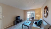 This single-floor unit at St Francis Apartments is designed for comfortable everyday living, with a thoughtful layout that connects key living spaces seamlessly. The living room serves as the heart of the home, featuring soft carpeting, warm neutral-toned walls, a textured ceiling, and a large sliding glass door that opens to a private balcony, filling the space with natural light and outdoor views. The kitchen is efficiently designed with rich wood cabinetry, granite-style countertops, a double-basin sink, and black appliances including an electric range, providing ample workspace for cooking and meal preparation. The unit includes two well-sized bedrooms, each finished with plush carpet and large windows dressed with vertical blinds that allow for generous natural light and views of the surrounding greenery. The primary bedroom features a sliding glass door to an outdoor area, while the secondary bedroom benefits from a broad window framing lush outdoor scenery. The bathroom is cleanly appointed with tile flooring, a tub and shower combination with tasteful tile surround, and a wood-toned vanity with a stone-finish countertop. Throughout the unit, the consistent use of warm, neutral tones and carpet flooring creates a cohesive and inviting atmosphere.
