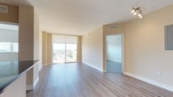 This well-appointed single-floor unit offers a clean, contemporary aesthetic throughout, with warm neutral tones and durable hardwood-style flooring that flows seamlessly across the living spaces. The open-concept living and dining area is generously proportioned, bathed in natural light from large floor-to-ceiling sliding glass doors that lead to a private balcony overlooking expansive city views — an ideal setting for both relaxing and entertaining.

The galley-style kitchen is efficiently designed, featuring rich wooden cabinetry, bold black granite countertops, stainless steel appliances including a range and built-in microwave, and a double sink — providing ample workspace and storage for everyday cooking.

Two well-sized bedrooms each benefit from roller-shade windows that frame open outdoor views, allowing natural light to fill the spaces while maintaining privacy. The clean white walls and hardwood-style flooring give each room a calm, versatile atmosphere.

The unit includes two bathrooms: one featuring a glass-enclosed shower with a granite-topped vanity, and a second with a full soaking tub and tub-shower combination accented by a decorative mosaic tile border. Both bathrooms are finished with white cabinetry, granite countertops, and clean tile flooring, maintaining a consistent modern feel throughout the entire space.