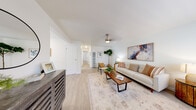 This single-floor residence offers a clean, contemporary aesthetic throughout, characterized by light wood-style flooring, crisp white walls, and abundant natural light that flows through multiple windows with blinds. The living room is a welcoming space anchored by a ceiling fan, neutral-toned furnishings, and a statement wall piece, creating a calm and inviting atmosphere. A dedicated dining area sits adjacent, bathed in natural light and providing an ideal setting for everyday meals or entertaining. The kitchen is thoughtfully designed with white shaker-style cabinetry, grey quartz countertops, and a full suite of stainless steel appliances including a gas range, over-the-range microwave, dishwasher, and refrigerator. Light wood-style flooring and a window above the sink add to the kitchen's bright, functional character. The residence includes two bedrooms, each finished with ceiling fans and large windows that invite natural light. One bedroom features mirrored sliding closet doors, adding depth to the space. The full bathroom is outfitted with a white vanity, grey countertop, a tub-shower combination, and wood-style flooring, maintaining the consistent, modern style found throughout the home. Overall, the space presents a cohesive, light-filled interior with practical finishes and a comfortable, residential feel.