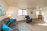 This single-floor unit offers a practical and comfortable layout designed to maximize livable space. The living room serves as the central gathering area, featuring plush carpeting, a textured ceiling, and a large window that allows natural light to fill the room. The open and airy feel is reinforced by clean white walls and warm wood-toned trim, creating a welcoming atmosphere.

The galley-style kitchen is efficiently arranged with warm wood cabinetry, granite-look countertops, a double basin sink, and white appliances including a refrigerator and electric range. The kitchen opens directly into a cozy dining nook, framed by a window overlooking the exterior, accommodating a bistro-style table and chairs ideal for casual meals.

The unit includes three carpeted bedrooms, each offering a quiet retreat with textured ceilings and windows providing natural light. Two of the bedrooms feature standard closet configurations, while one includes a full-width sliding-door closet for ample storage.

The bathroom is finished with a wood-framed vanity mirror, single-sink vanity with storage cabinetry below, and a shower-tub combination. Tile-style flooring completes the functional space. Throughout the unit, consistent neutral tones and warm wood accents contribute to a cohesive, understated aesthetic.