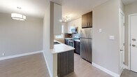 Located at 18 Avenue SW in Calgary's vibrant Mission neighbourhood, this one-bedroom, one-bathroom unit offers a thoughtfully designed layout that maximizes every inch of its compact footprint. Light-toned laminate flooring flows consistently throughout the space, complementing neutral warm-grey walls that create a clean, cohesive aesthetic.

The open-concept kitchen and living area form the heart of the unit. The kitchen is well-appointed with two-tone cabinetry—combining crisp white upper cabinets and dark walnut-finish lower cabinets—paired with light quartz countertops, a tile backsplash, stainless steel appliances including a refrigerator, electric range, and microwave, and a double undermount sink. A peninsula counter provides a natural divide between the kitchen and living area.

The bedroom features a standout built-in low cabinet unit beneath a large window that frames city skyline views, adding both functional storage and a distinctive architectural element. A pendant light fixture adds warmth to the space.

The bathroom is finished with a dark wood vanity, quartz countertop, undermount sink, and a glass-enclosed shower, maintaining the unit's modern design language throughout. The overall ambiance is clean, contemporary, and efficiently organized.