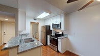 This single-floor residence offers a thoughtfully designed open-concept layout that connects the kitchen and living area seamlessly. The kitchen is well-appointed with white shaker-style cabinetry, granite countertops, a double stainless steel sink, and a full suite of stainless steel appliances including a refrigerator, electric range, and over-the-range microwave. A skylight above the kitchen provides an additional source of natural light, brightening the workspace. The kitchen opens directly to the living area, which features warm hardwood-style flooring, a ceiling fan with light fixture, and a sliding door or vertical-blind window treatment that allows natural light to filter in.

The bedrooms are finished with neutral-toned carpet and warm beige walls, offering a calm and comfortable atmosphere. Each bedroom includes a closet, with at least one featuring a walk-in or reach-in shelved closet. Windows in the bedrooms provide outdoor views and natural light.

The bathroom is finished with tile flooring, white cabinetry, granite countertops, and a tub-shower combination. Throughout the unit, textured ceilings and clean white trim contribute to a cohesive, well-maintained aesthetic.