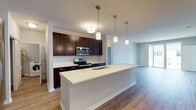 This two-story residence in Romeoville, Illinois presents a thoughtfully designed layout with modern finishes throughout. The main level centers around an open-concept kitchen and living area, where rich dark-espresso cabinetry contrasts elegantly with bright white countertops. A generously sized kitchen island with an undermount sink serves as the focal point, illuminated by a series of pendant lights suspended at varying heights. Stainless steel appliances, including a French door refrigerator, electric range, and built-in microwave, complete the well-appointed kitchen. Wood-look flooring flows throughout the main living areas, contributing to a warm and cohesive aesthetic. A dedicated laundry area with an in-unit washer is conveniently tucked off the kitchen corridor. The upper level features carpeted bedrooms that offer a comfortable retreat, with windows that allow natural light to filter in. The bathrooms are finished with dark vanity cabinetry, white countertops, and light wood-look flooring, with the primary bath including a tall linen tower for additional storage. Neutral wall tones and clean white trim carry throughout, lending a fresh and move-in-ready feel to the entire home.