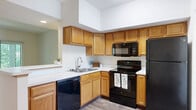 Located at 51 Great Trail Circle in Pickerington, Ohio, this one-bedroom, one-bathroom unit offers a well-organized, single-floor layout designed for comfortable everyday living. The open-concept kitchen is a standout feature, equipped with warm oak cabinetry, a full suite of black appliances including a refrigerator, range, built-in microwave, and dishwasher, and a peninsula with a breakfast bar that seamlessly connects to the living area. Light hardwood-style flooring runs throughout the kitchen and main hallway, adding a clean, modern look. The living area features soaring vaulted ceilings and a large window that invites natural light and views of the surrounding greenery. The bedroom is generously sized with plush carpeting, a window overlooking the outdoors, and direct access to a spacious walk-in closet outfitted with wire shelving and hanging rods for ample storage. The full bathroom features an oak vanity with a large mirror, bright vanity lighting, and hardwood-style flooring. A dedicated in-unit laundry area houses a full-size top-loading washer and dryer with overhead wire shelving, adding a highly practical amenity. This unit combines functional design with comfortable finishes throughout.