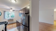 Located at 413 E Main Street in Bay Shore, NY, Bayshore Gardens presents a thoughtfully laid-out single-floor residence that combines classic details with modern updates. Warm hardwood flooring runs throughout the living spaces, lending a cohesive and inviting feel to the home.

The galley-style kitchen is well-appointed with rich, dark shaker cabinetry extending to the ceiling, light stone-look countertops, and a full suite of stainless steel appliances including a gas range, over-the-range microwave, and French door refrigerator. A window at the end of the kitchen fills the space with natural light.

The living area is generously sized and bright, featuring large windows that frame views of the surrounding greenery, with baseboard heating and crown molding adding to the refined character of the room. Additional rooms offer flexible use as bedrooms or living spaces, each continuing the hardwood flooring and neutral palette. One bedroom includes a built-in closet for convenient storage.

The bathroom is clean and bright, finished with white subway tile surrounding a full soaking tub and shower combination, brushed nickel fixtures, and a window for natural ventilation. The overall ambiance of the space is light, airy, and move-in ready.